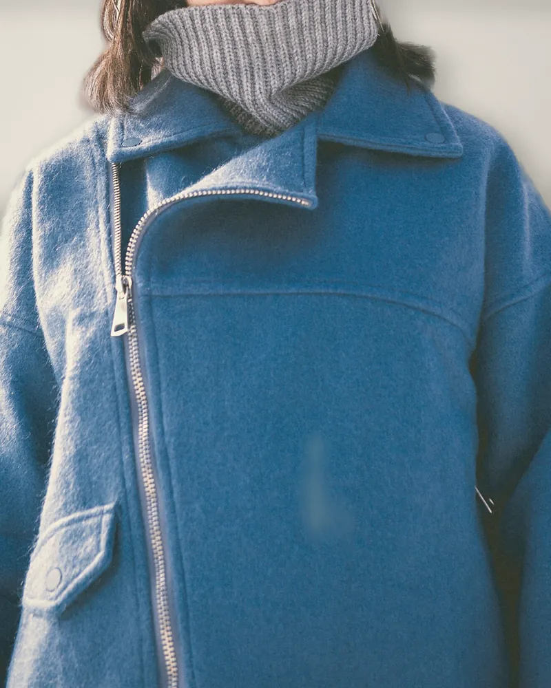 A cobalt blue wool coat with an off-centre zip and a high funnel neck, worn over a grey knitted snood