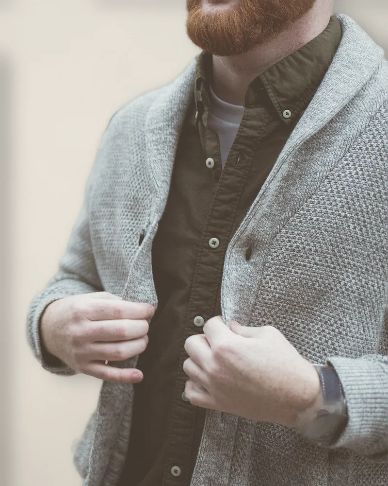 Hands doing up a grey shawl-collar cardigan worn over a dark green shirt