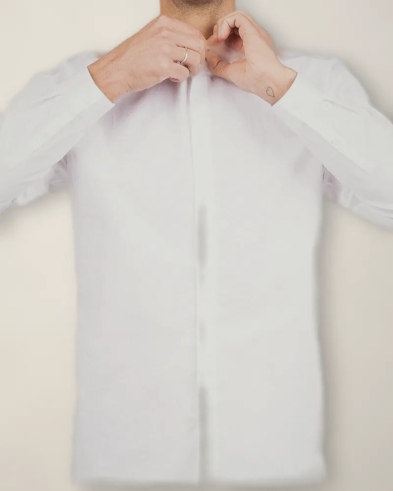 Hands doing up the top button of a plain white cotton poplin shirt
