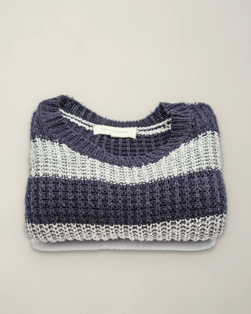 A navy and pale grey striped jumper in a waffle knit, folded, on the paper of the shop's back wall