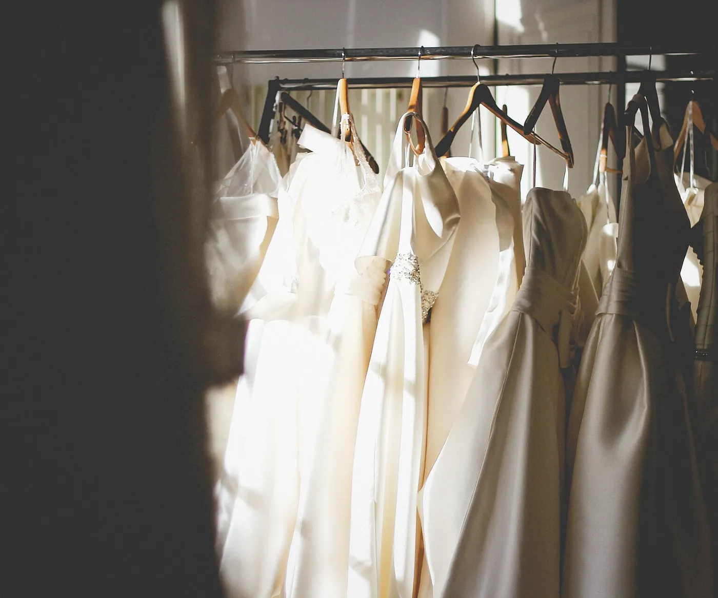 Cream and white dresses on hangers along a dark rail, afternoon light falling across them
