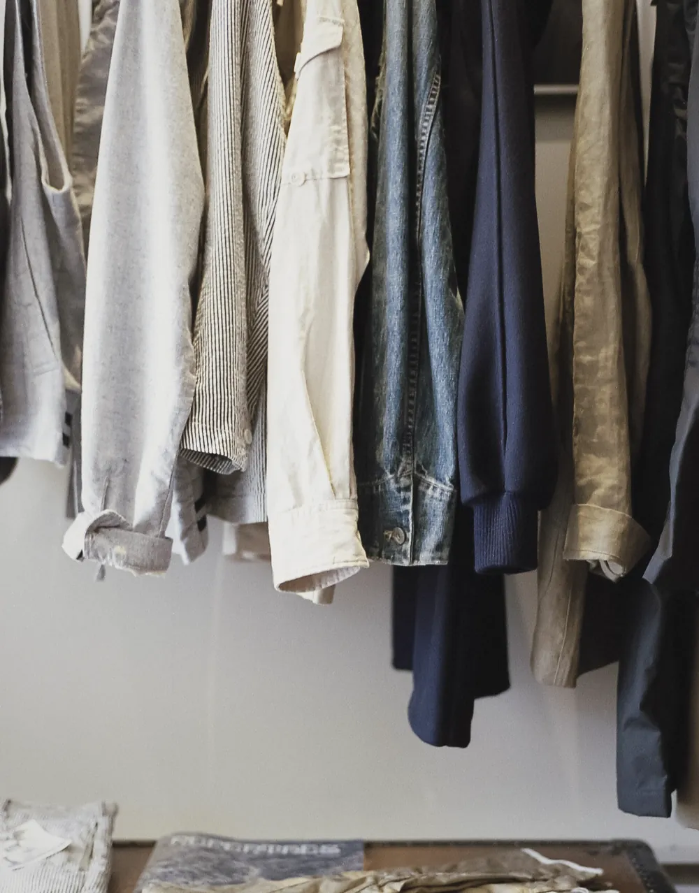Shirts and jackets in greys, denim and navy hanging above a wooden trunk