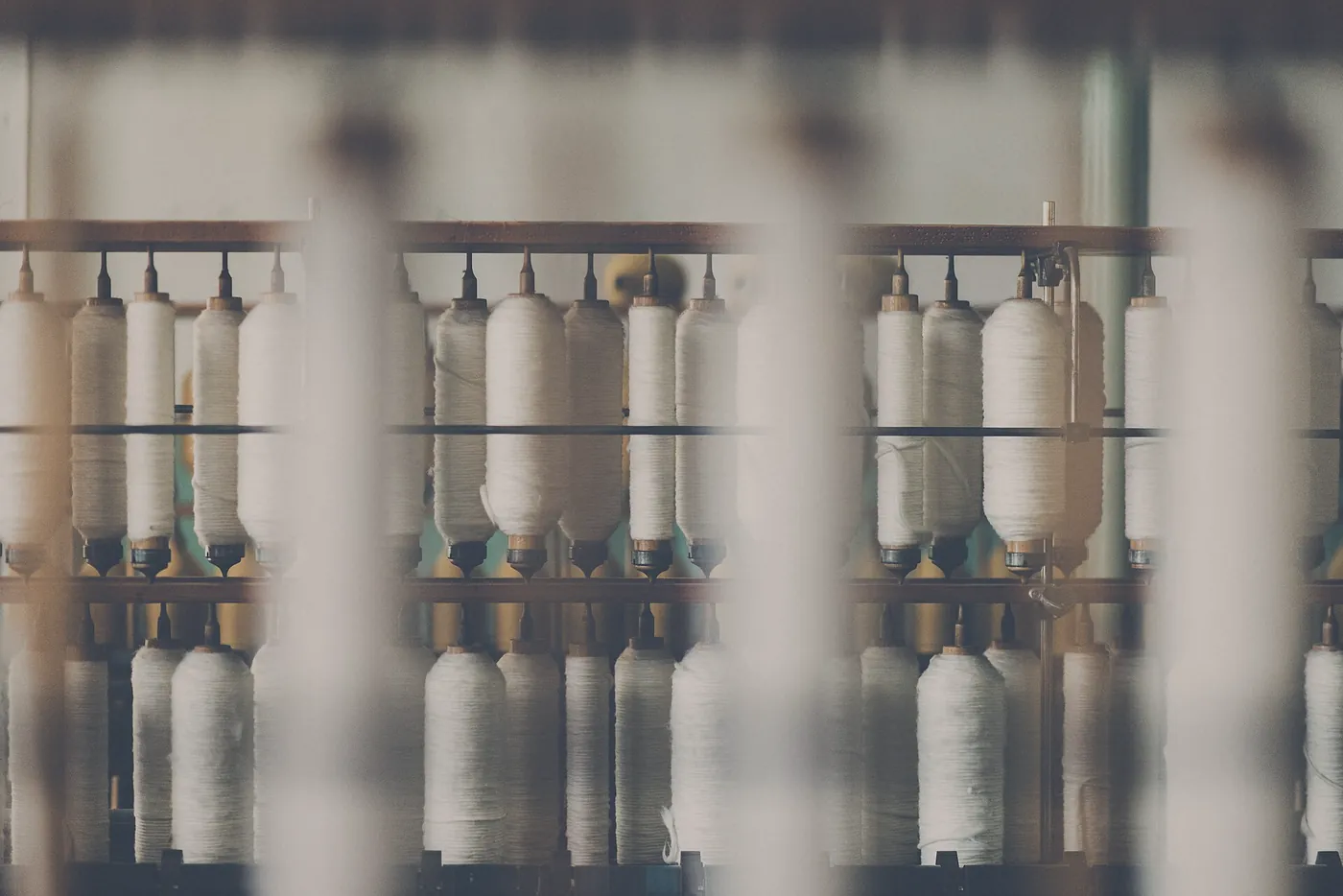 Rows of undyed cotton on bobbins in a mill, out of focus