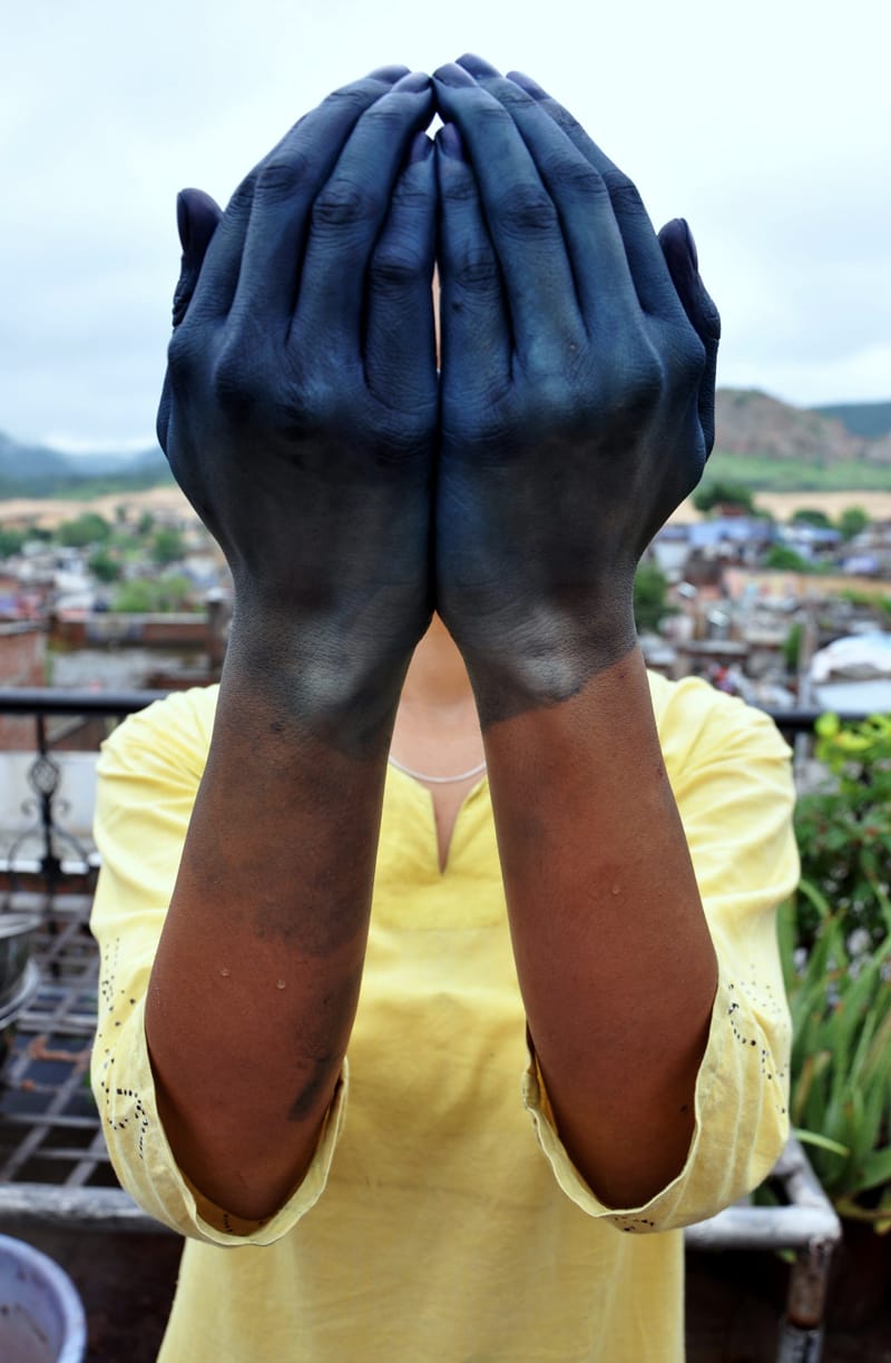 A person holding up hands stained deep blue with indigo
