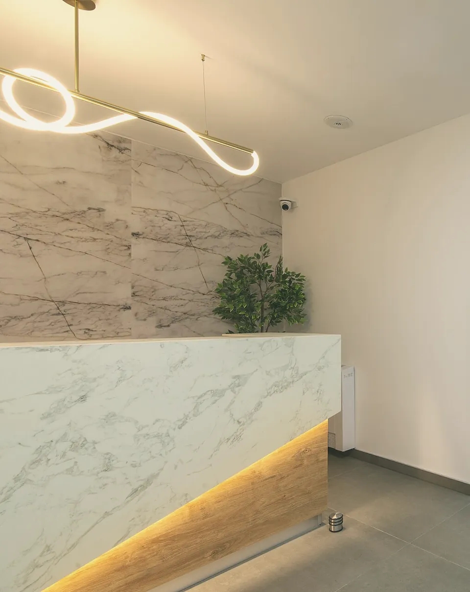 The reception desk: white marble, a warm light underneath, a plant at the end.