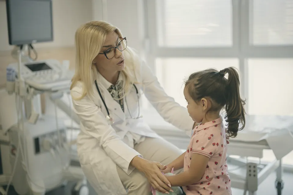 A doctor kneeling to examine a little girl's tummy while the girl watches.