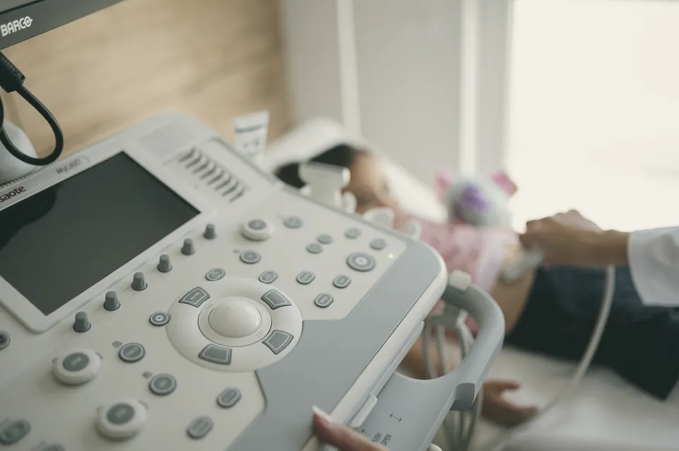 A child lying on the couch during an ultrasound scan, a soft toy beside her.