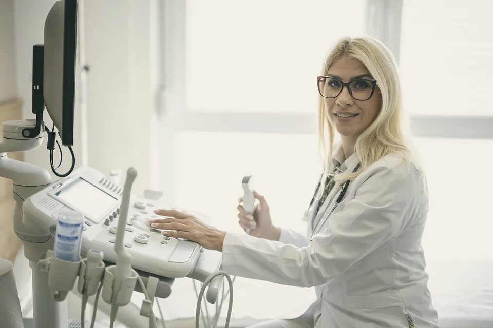A doctor at the ultrasound machine, probe in hand, smiling towards the couch.