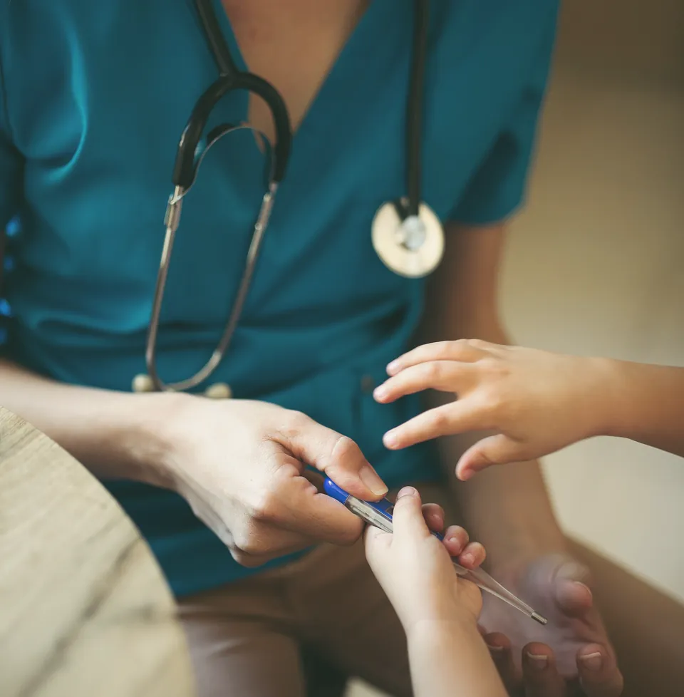 A nurse in teal scrubs holding a child's hands during a vaccination.