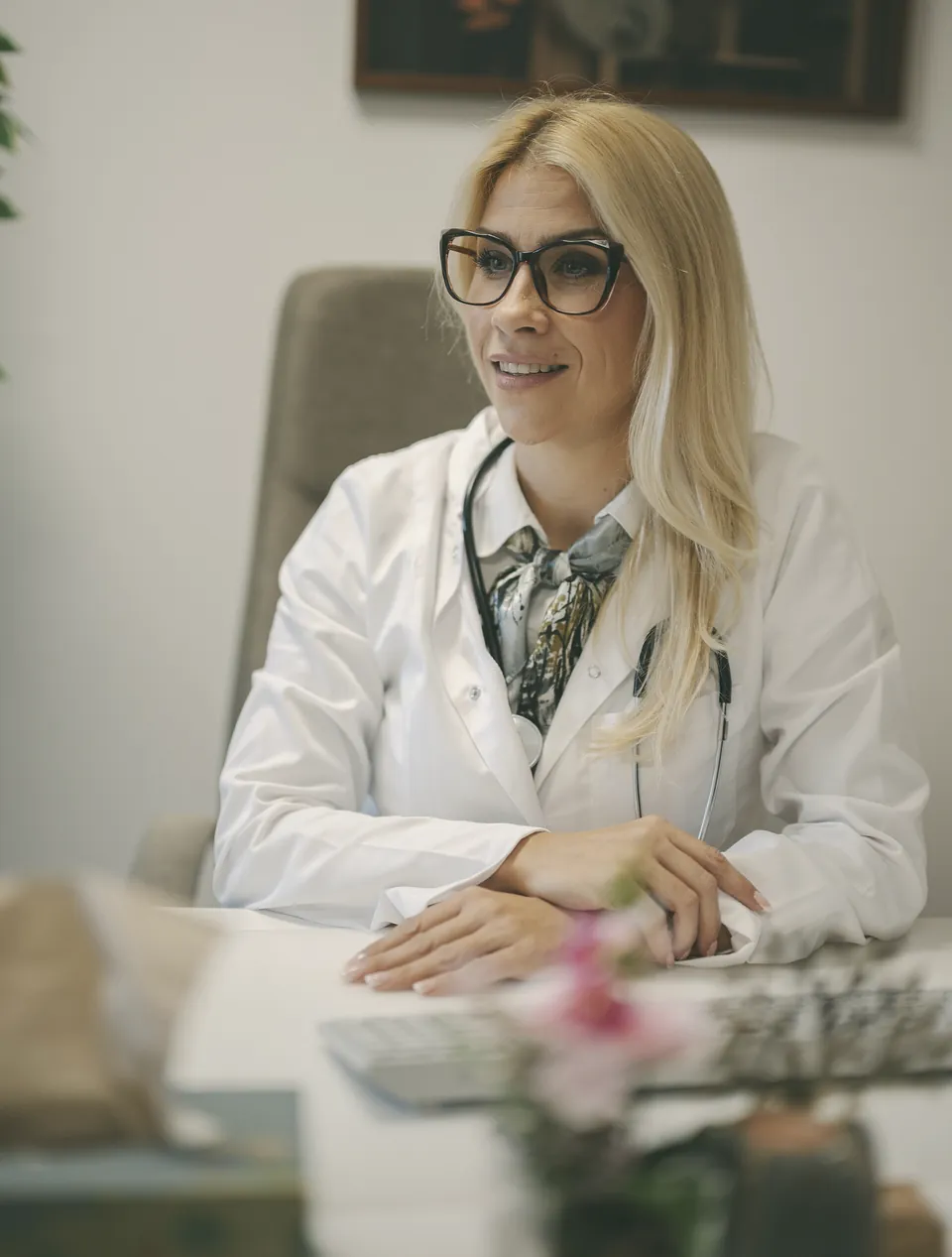 A doctor sitting at her desk, turned towards the patient, hands folded.
