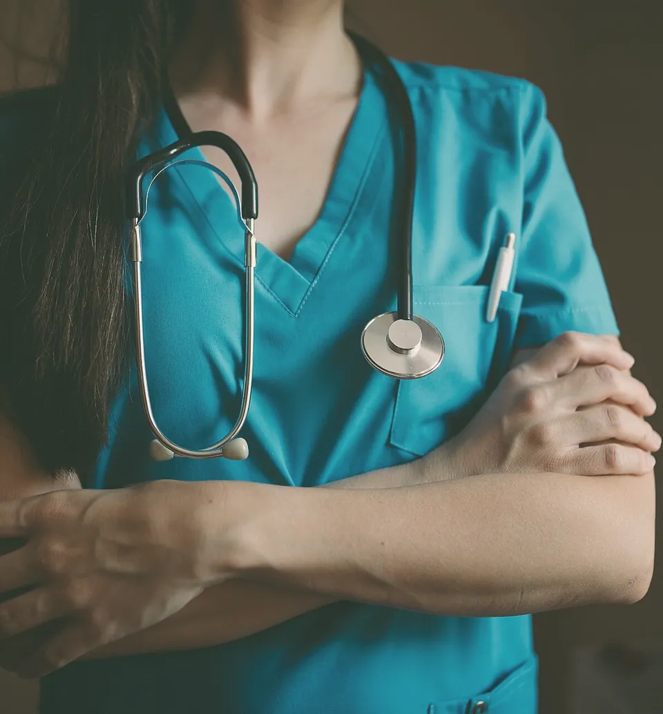 A doctor in teal scrubs with a stethoscope round her neck, arms folded.