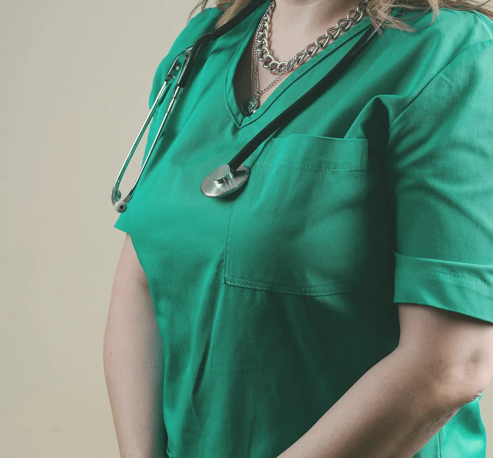 A doctor in green scrubs with a stethoscope, hands clasped.