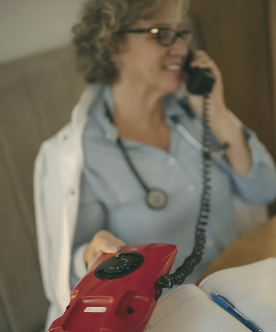 A doctor on the phone at her desk, a notebook open in front of her.