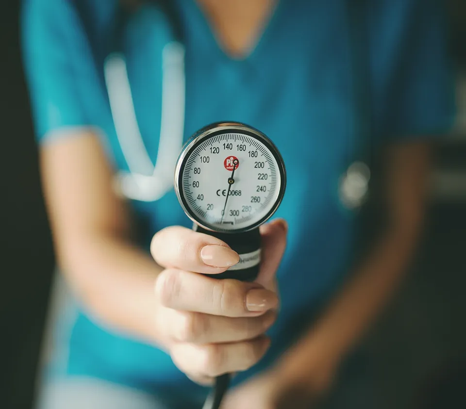 A blood pressure gauge held up in a nurse's hand, teal scrubs behind it.