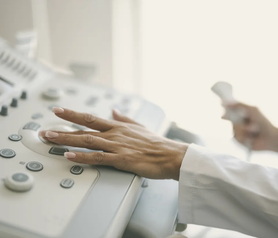 A hand resting on the ultrasound controls while the other holds the probe.