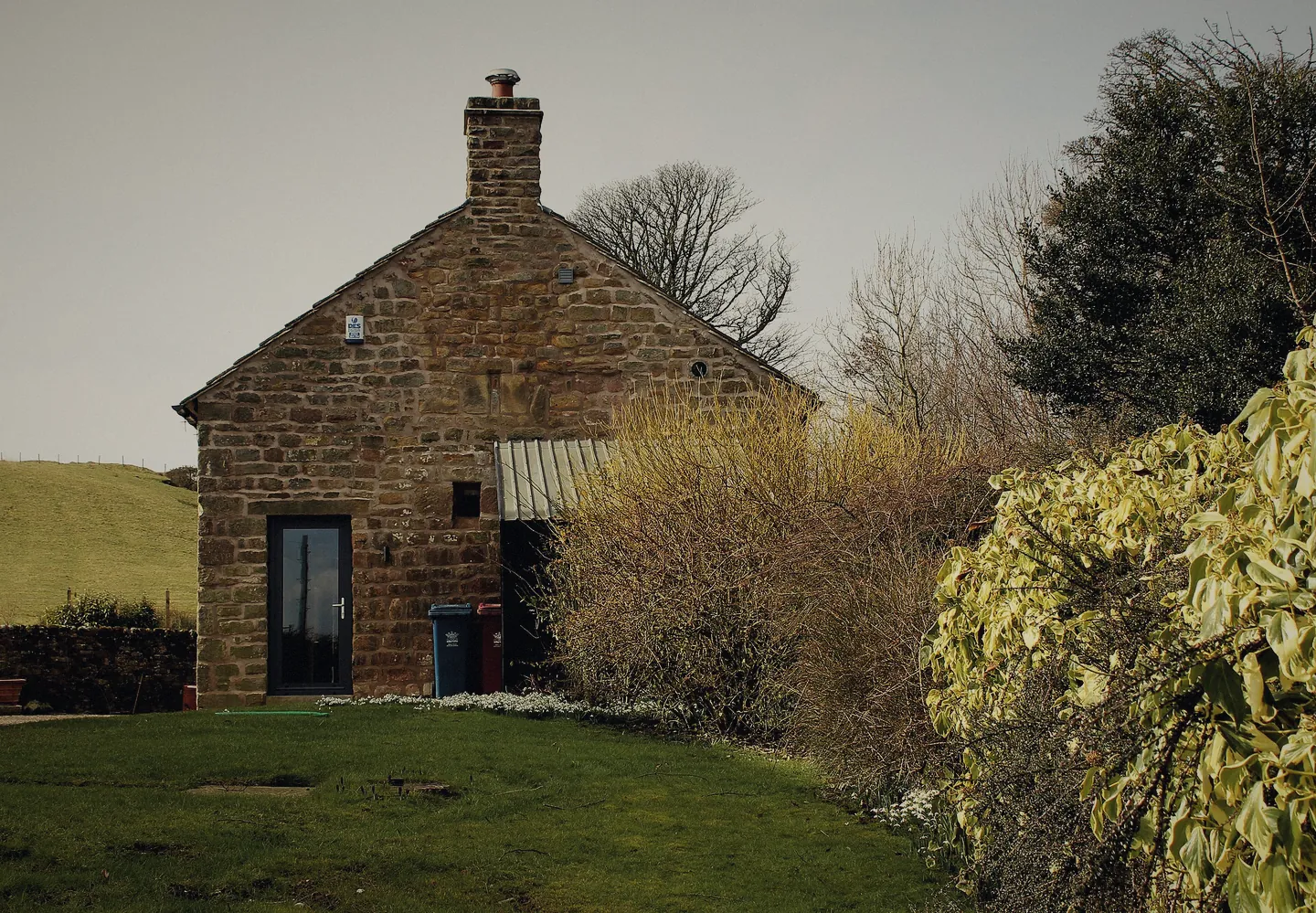 A stone camping barn with a slate roof and a chimney, a lawn in front