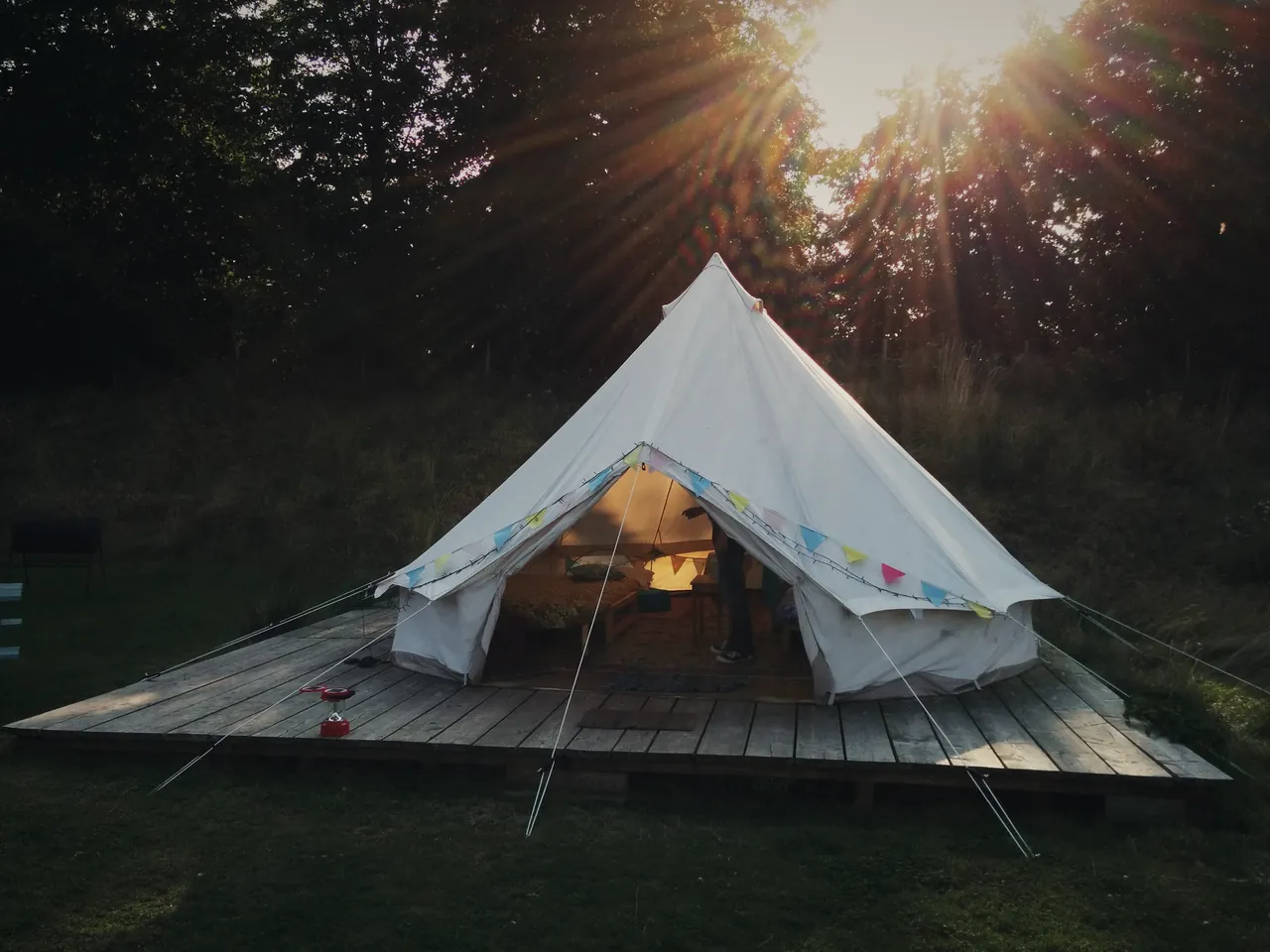 A bell tent on a timber deck at sunset, door open, bunting across the front