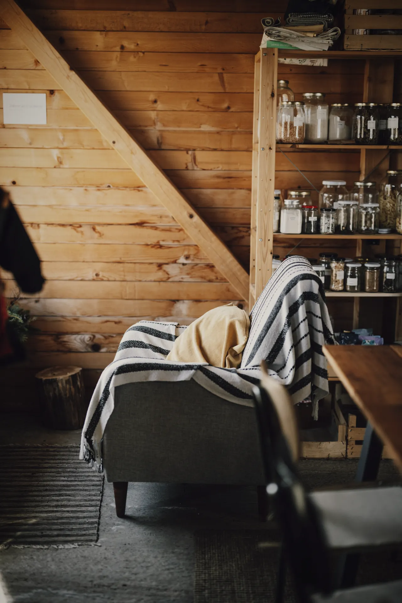 Inside a pine cabin: an armchair with a striped blanket and shelves of jars