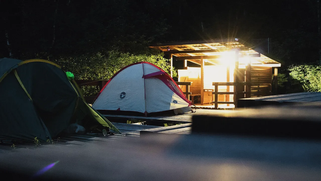 Two tents beside a lit timber shelter at night