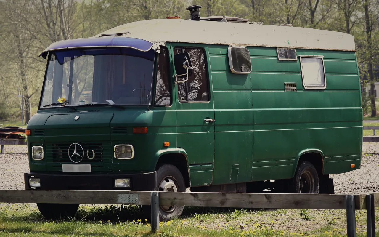 A green campervan parked on grass in front of trees