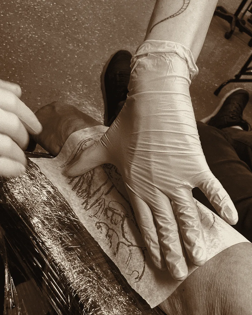 Gloved hands pressing a stencil onto a client’s forearm