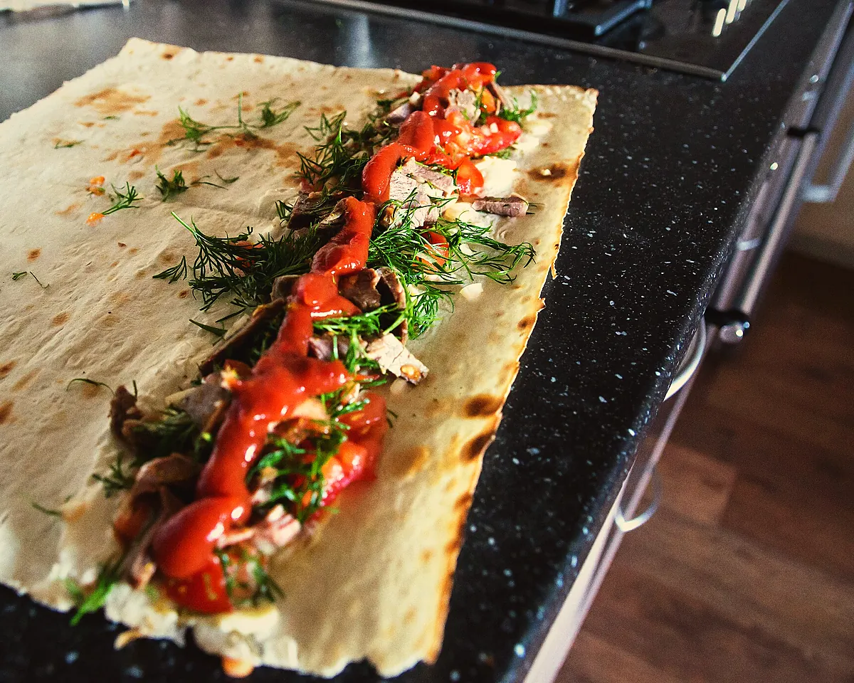 A lavash being filled with shaved meat, herbs and sauce