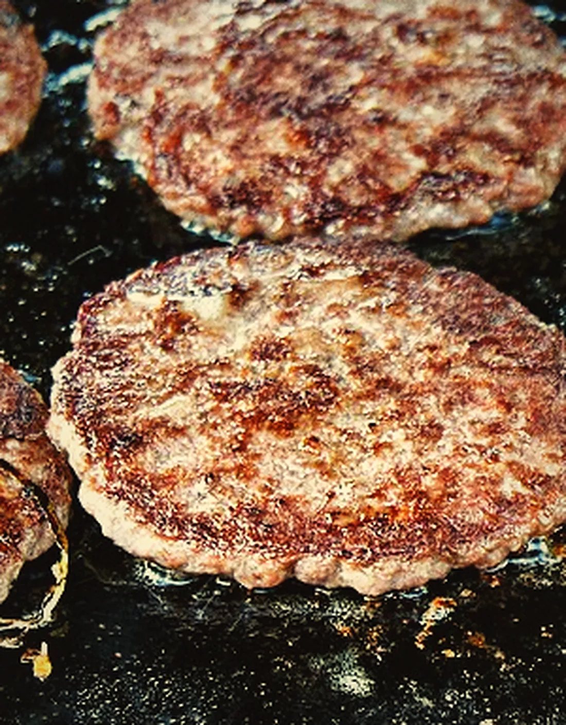 Rows of burger patties searing on a black flat-top