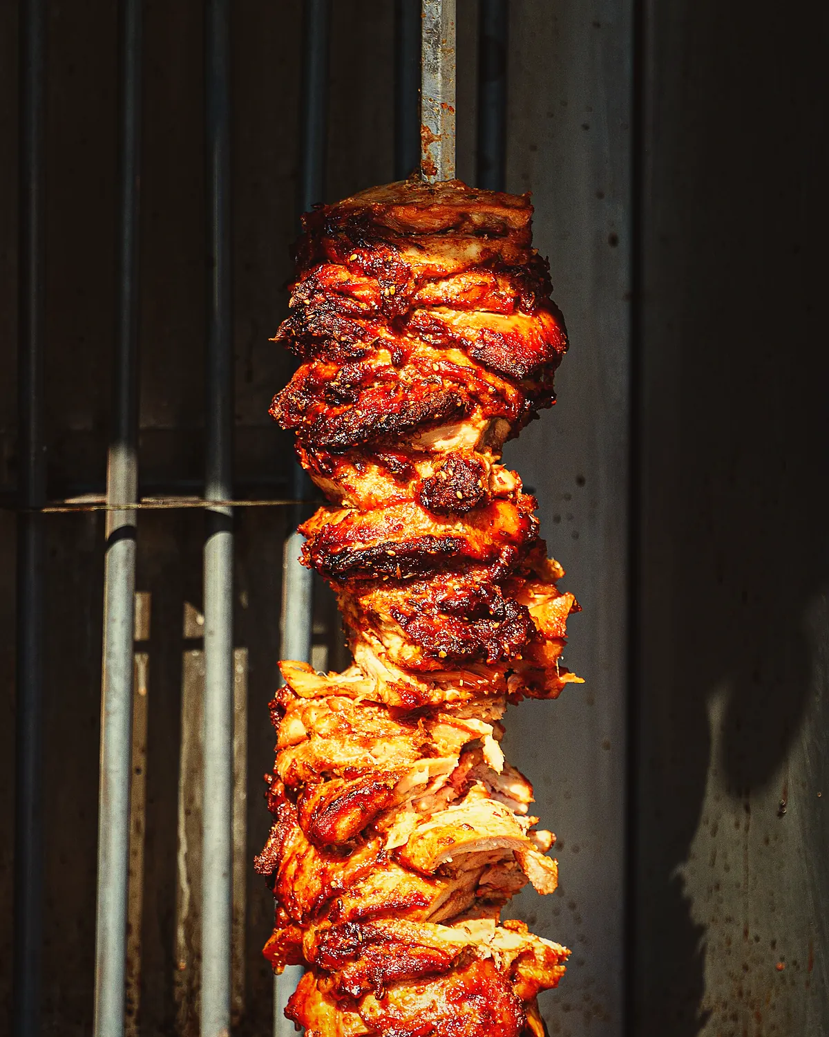 Chicken stack on the spit, edges charred, against the grill bars