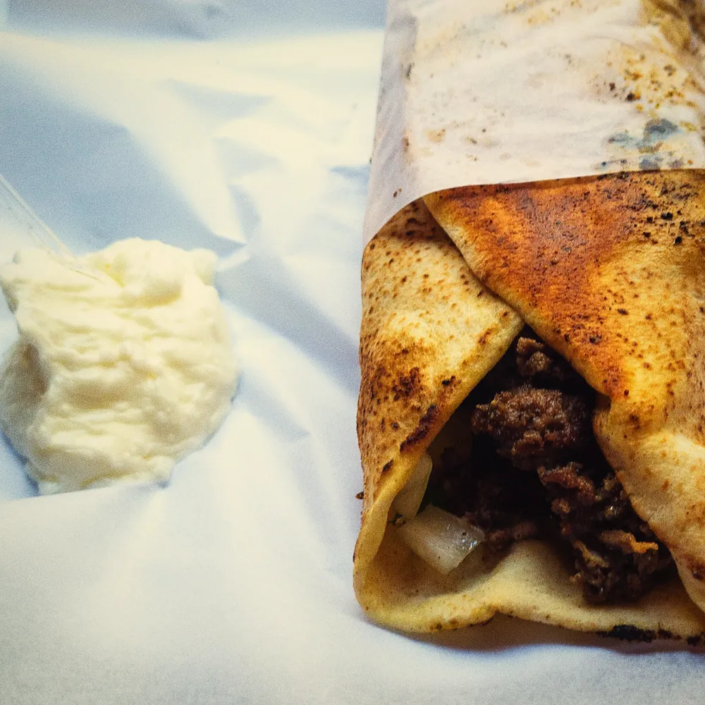 A spoon of toum beside a wrap in greaseproof paper