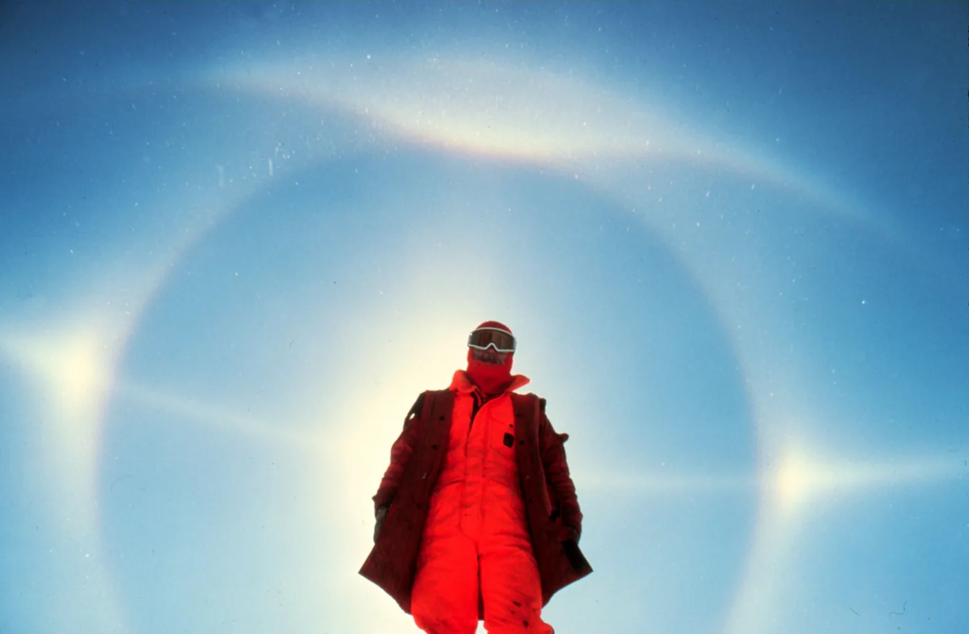 A 22° halo with sun dogs and a parhelic circle over the South Pole station, a person in red standing in front of the Sun
