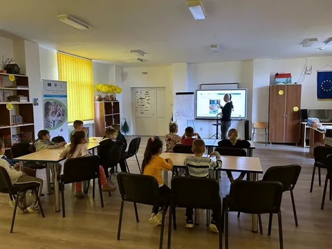 Sala polivalentă cu rafturi de cărți și mese, în timpul unei activități cu preșcolarii