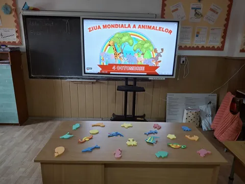 Clasă cu ecran interactiv pe care scrie Ziua Mondială a Animalelor și figurine pe o masă