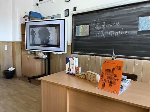 Sală de clasă cu tablă verde, ecran interactiv și machete pe catedră