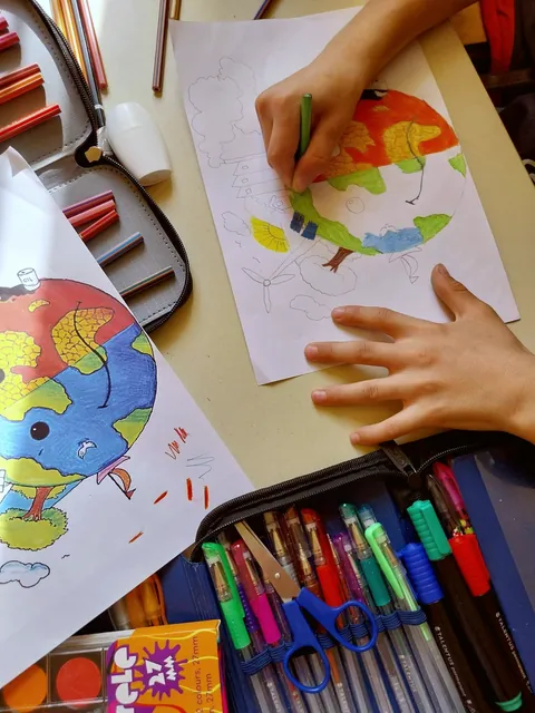 Mâini de copii desenând planeta Pământ cu creioane colorate