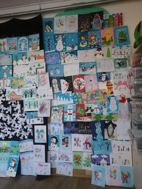 Detaliu din expoziția de desene de iarnă: oameni de zăpadă, case și brazi pe fond albastru