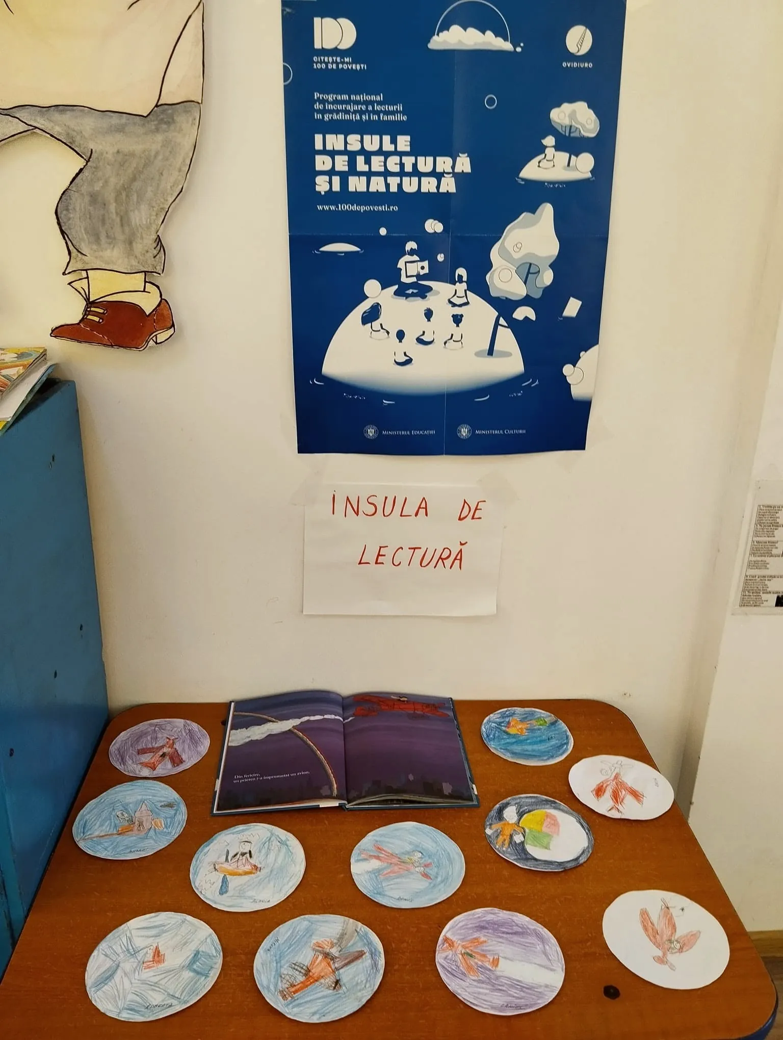 Afișul Insula de lectură și farfurii pictate de preșcolari pe o masă