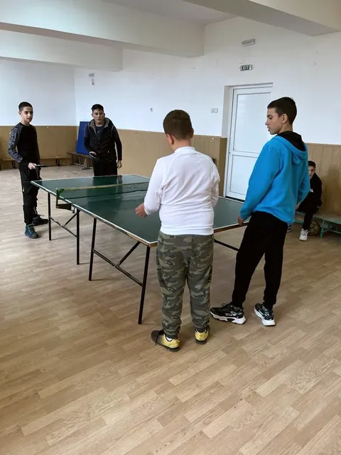 Elevi jucând tenis de masă într-o sală de sport luminoasă