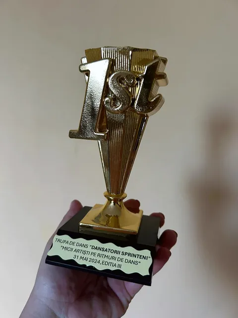 O mână ține un trofeu auriu pe care scrie 1st
