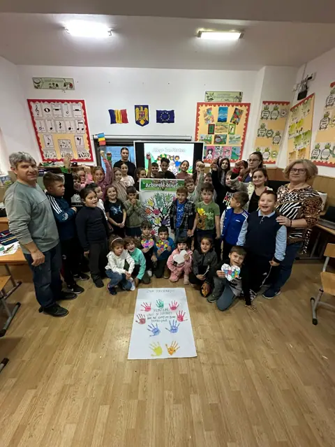 Ziua Internațională a Toleranței 2025, elevi și profesori în sala mare, cu panoul de palme colorate