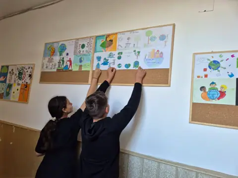 Elevi agățând desene pe holul școlii (din spate)