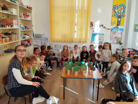 Sala de grupă a grădiniței, preșcolari în cerc cu plante
