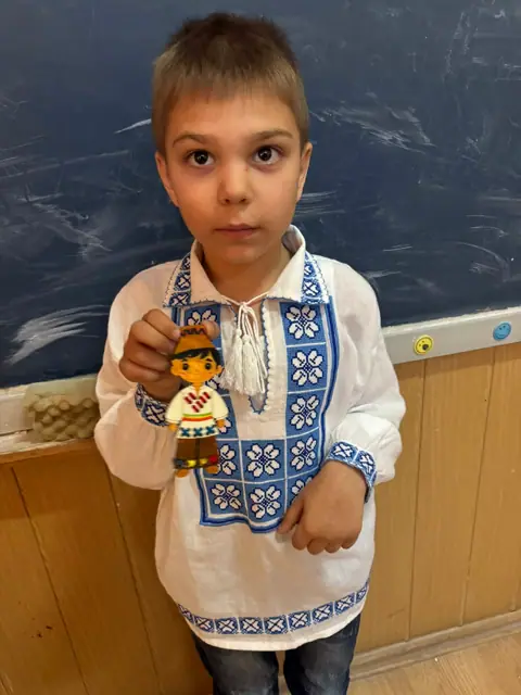 Elev în ie cu păpușă în port popular (portret)
